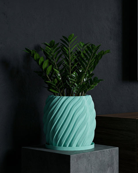 A ZZ plant in a light blue, spiraled planter pot sits atop a dark gray concrete stand against a dark gray wall.