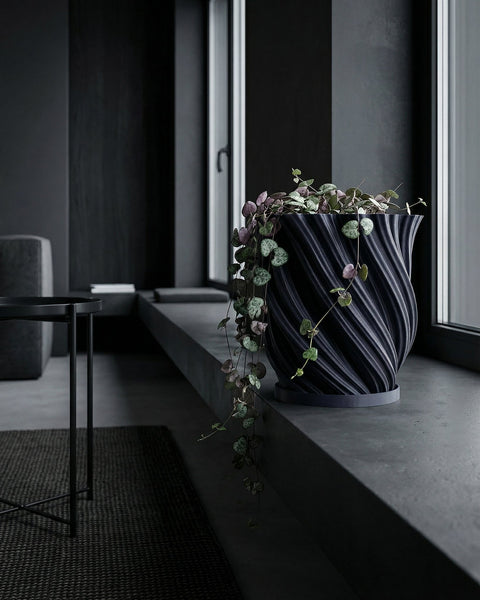A blue planter pot with a textured design sits on a wooden bench, filled with a lush green plant with unique leaf shapes.