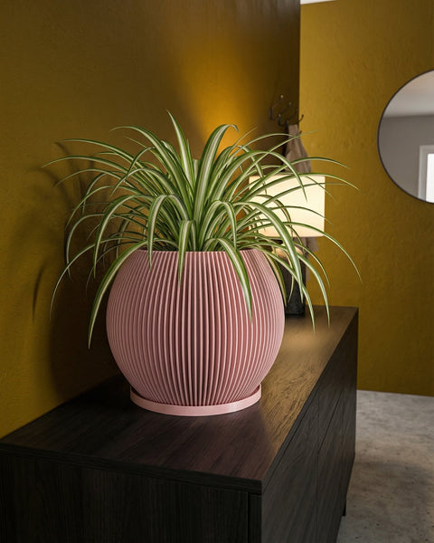 A pink planter pot with a spider plant sits on a dark wooden cabinet against a mustard-colored wall.