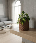 A brown planter pot with a green plant inside sits on a wooden table in a room with blue walls and a round mirror.