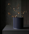 A dark blue ribbed planter pot with dried branches on a dark gray surface.