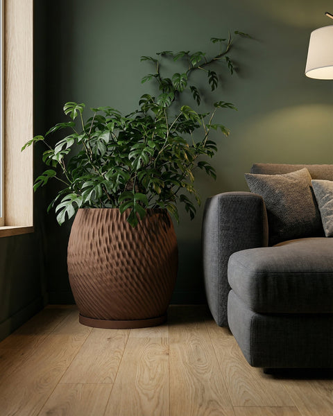 A brown textured planter pot with a green plant next to a gray couch on a wooden floor.
