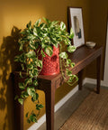 A vibrant pothos plant cascades from a red geometric planter on a wooden console table, adding a touch of nature to the room.