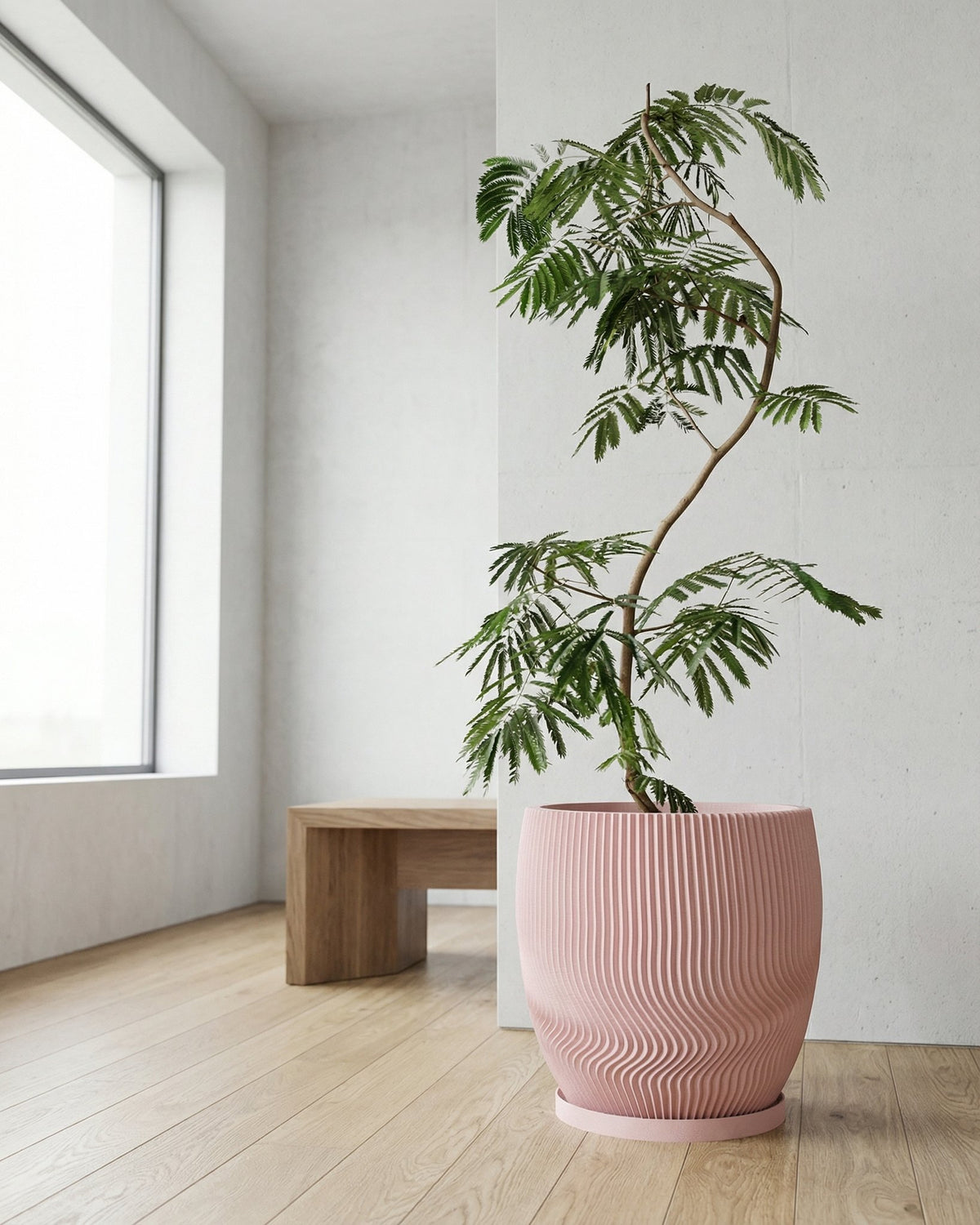 A pink planter pot with a green plant inside, sitting on a light wood floor next to a white wall.
