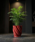 A red planter pot with a plant sits on a dark wooden bench in a room with dark green walls and a round gold mirror.