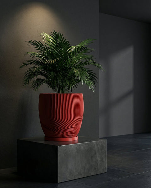 A vibrant red planter pot with a lush green plant sits atop a dark gray pedestal against a muted background.