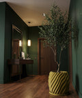 A green room with a wooden floor features a large potted plant in a unique, textured yellow planter pot.