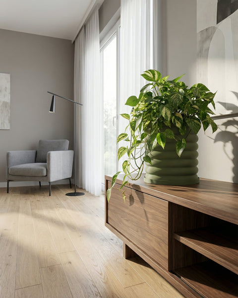A green planter pot with a plant sits on a wooden cabinet in a living room with a gray armchair and floor lamp.