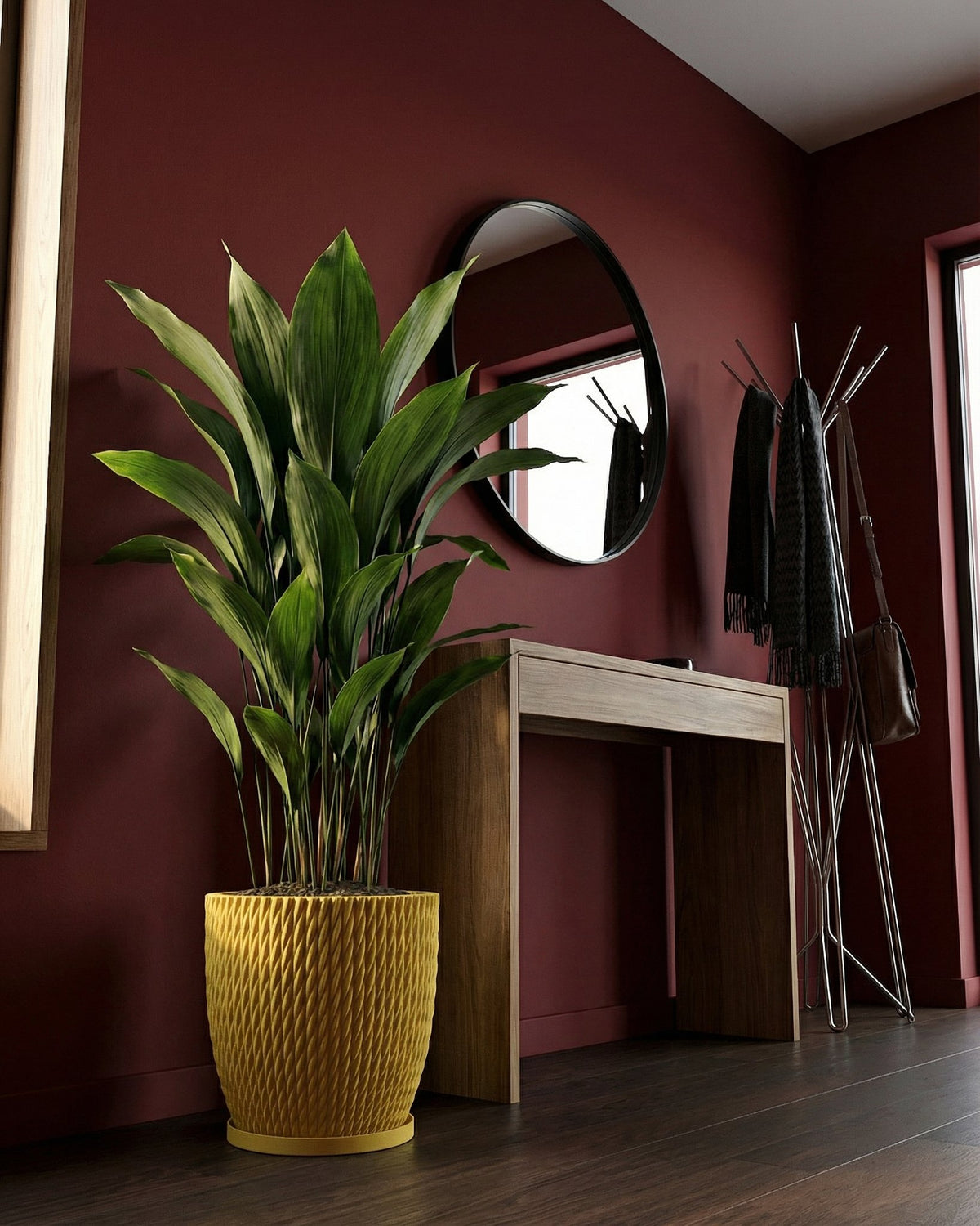 A large green plant sits in a textured yellow planter pot, next to a wooden table and a coat rack with scarves and a bag.