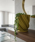 A yellow textured planter pot with a plant next to a gray couch and a round rug in a room with dark green walls.