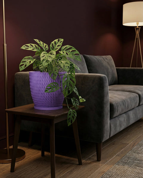 A purple planter with a plant on a wooden table next to a gray couch and a lamp.