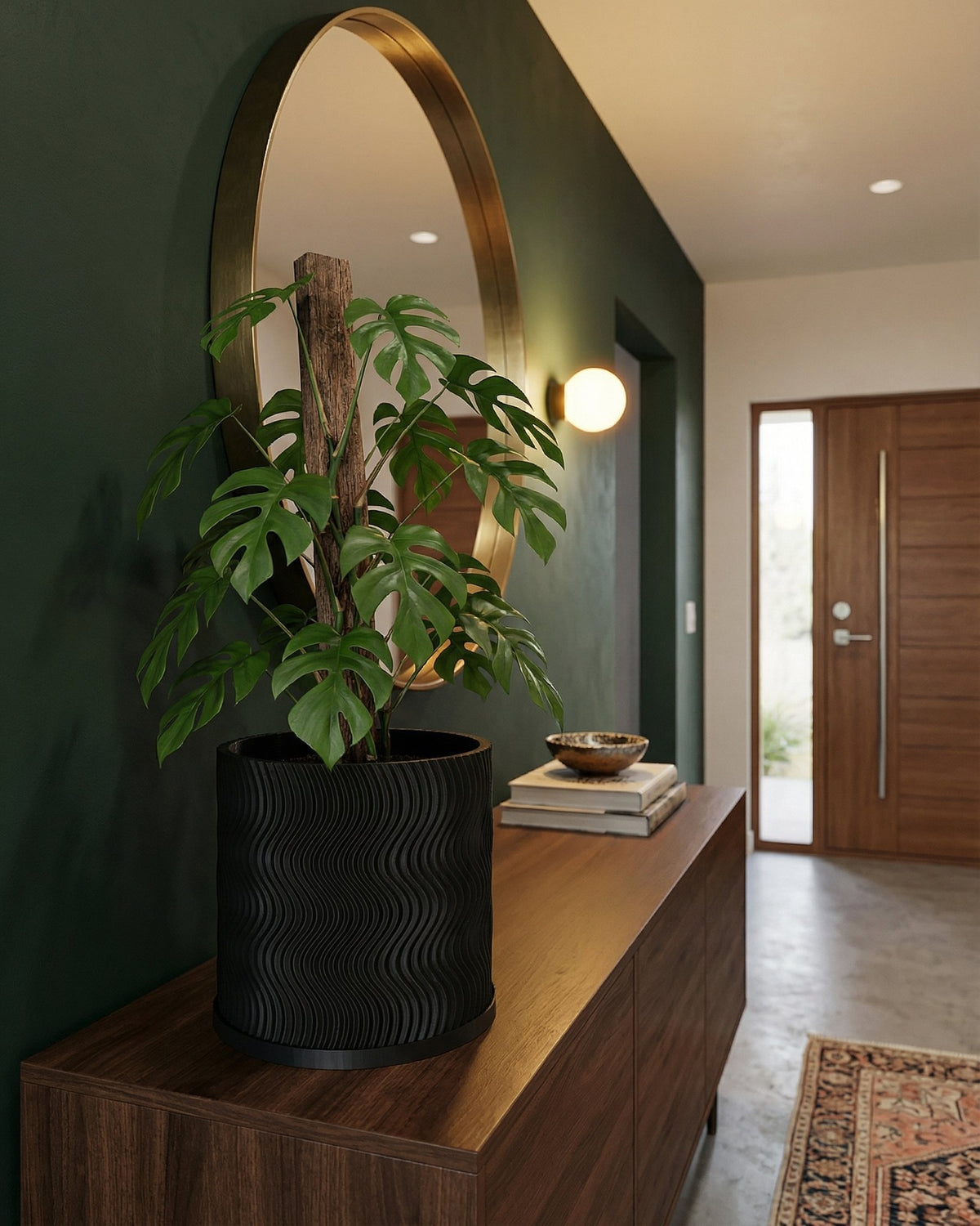 A black planter pot with a wavy design sits on a wooden cabinet, with a green plant inside. A round mirror and a doorway are in the background.