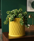 A bright yellow planter pot with a green plant sits on a white windowsill next to a window with sheer white curtains.