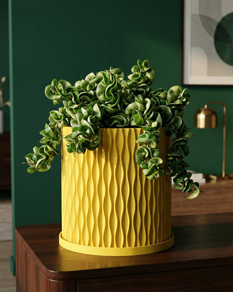 A bright yellow planter pot with a green plant sits on a white windowsill next to a window with sheer white curtains.