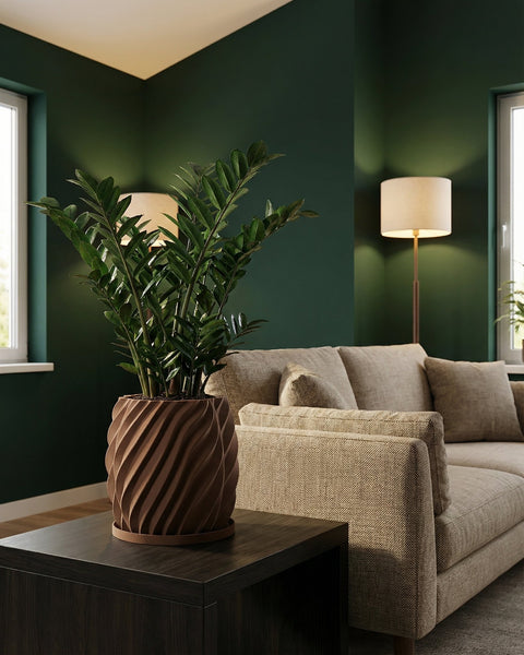A ZZ plant in a brown planter pot sits on a dark wood table next to a beige sofa in a room with dark green walls.