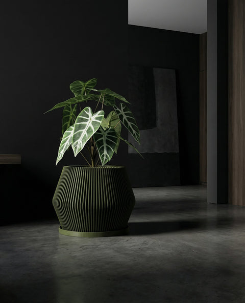 A green planter pot with a string of turtles plant sits on a wooden cabinet in a modern living room. The pot has a unique vertical slat design, and the plant's vines cascade down the side. The background includes a gray sofa, a patterned rug, and sheer curtains.