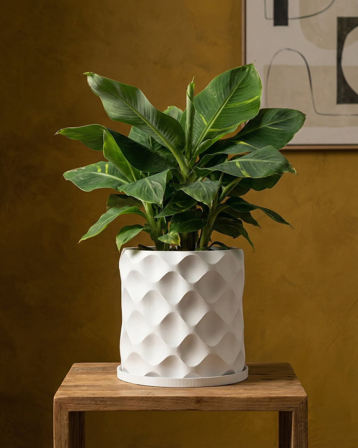 A white geometric planter pot with a green houseplant sits on a wooden table against a yellow wall.