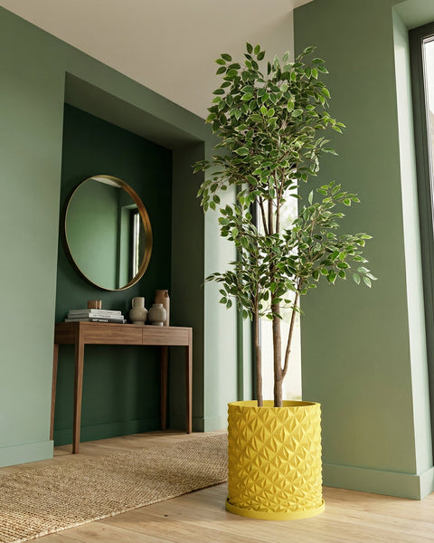 A tall ficus tree in a bright yellow geometric planter pot sits on a wooden floor in a green room.