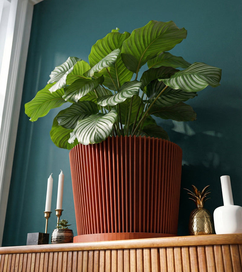 A terracotta planter pot with a diamond pattern holds a green plant on a marble-topped side table next to a gray sofa with a cream-colored throw.