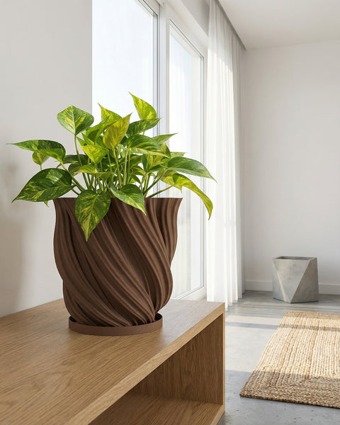 A brown textured planter pot with a green plant next to a gray couch on a wooden floor.