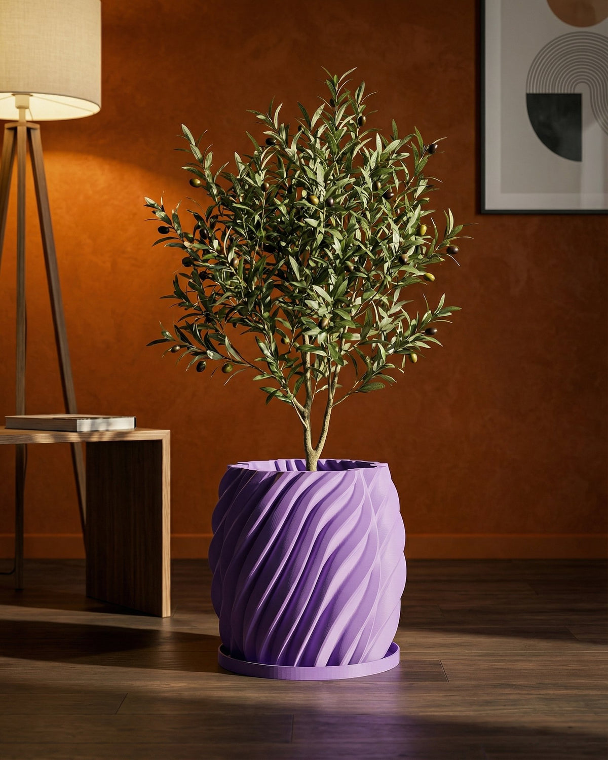 A small olive tree in a purple, swirling planter pot sits on a wooden floor in front of an orange wall.