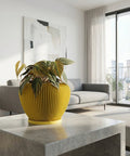 A yellow planter pot with a green plant sits on a gray concrete table in a modern living room.